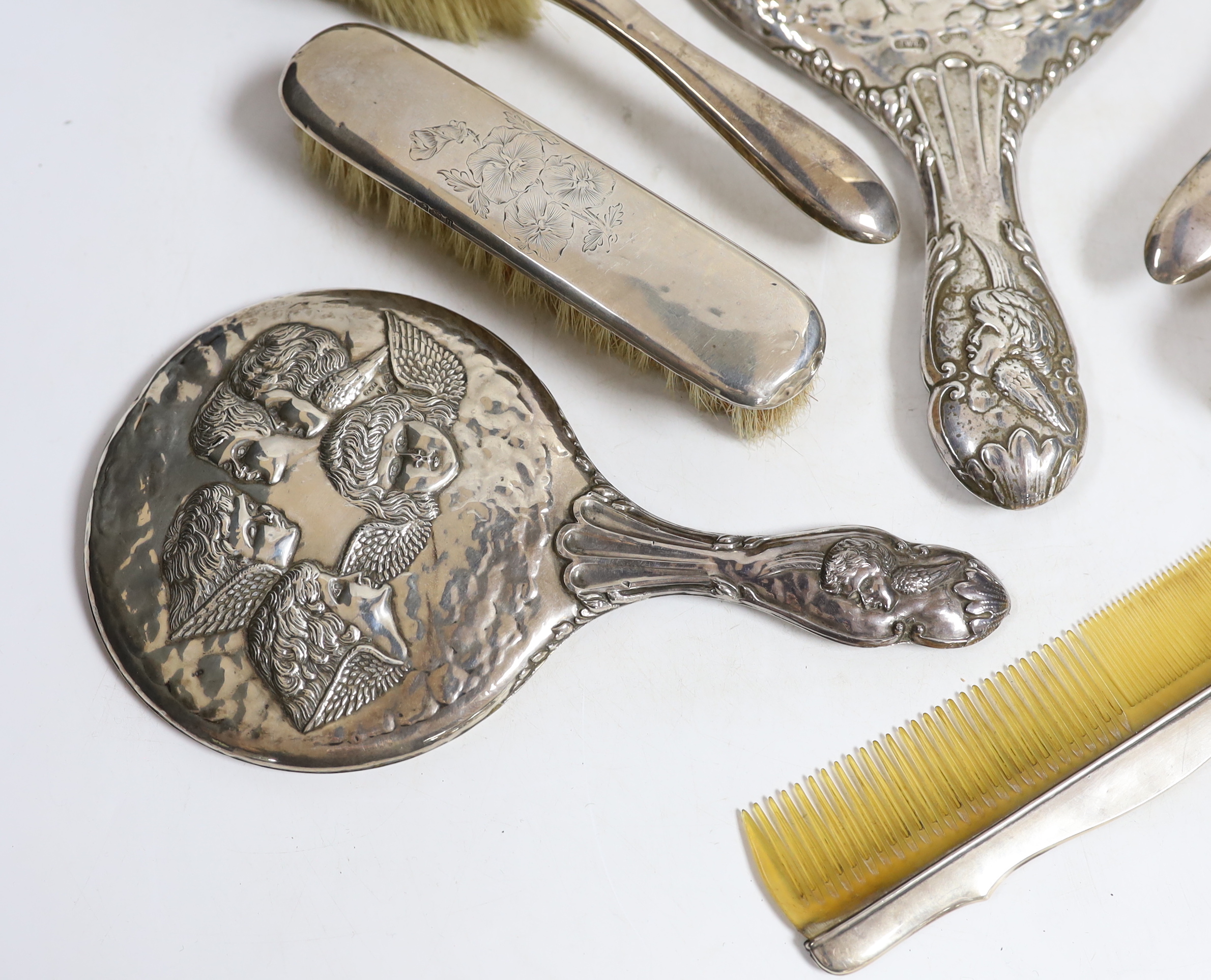 Two early 20th century repousse silver mounted hand mirrors with Reynold's Angels decoration, four silver mounted brushes and a comb.